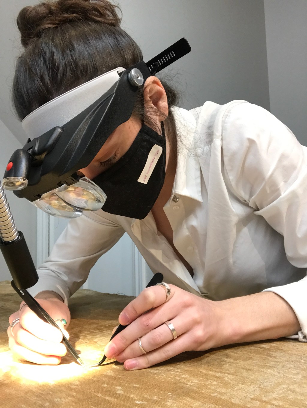 A conservator wearing optivisors leaning over a canvas to do tear repair with tweezers